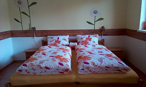 Izba č. 1 s kvetovanou posteľnou bielizňou pod margarétami na stene