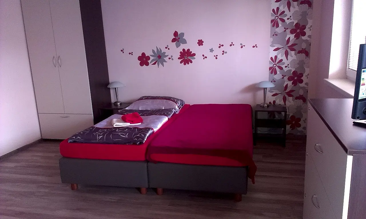 Posteľ s červeným prehozom a skriňa v izbe č. 11