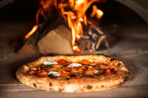 Pizza sa pečie v peci na drevo pri plápolajúcom ohni (ilustračná fotografia)